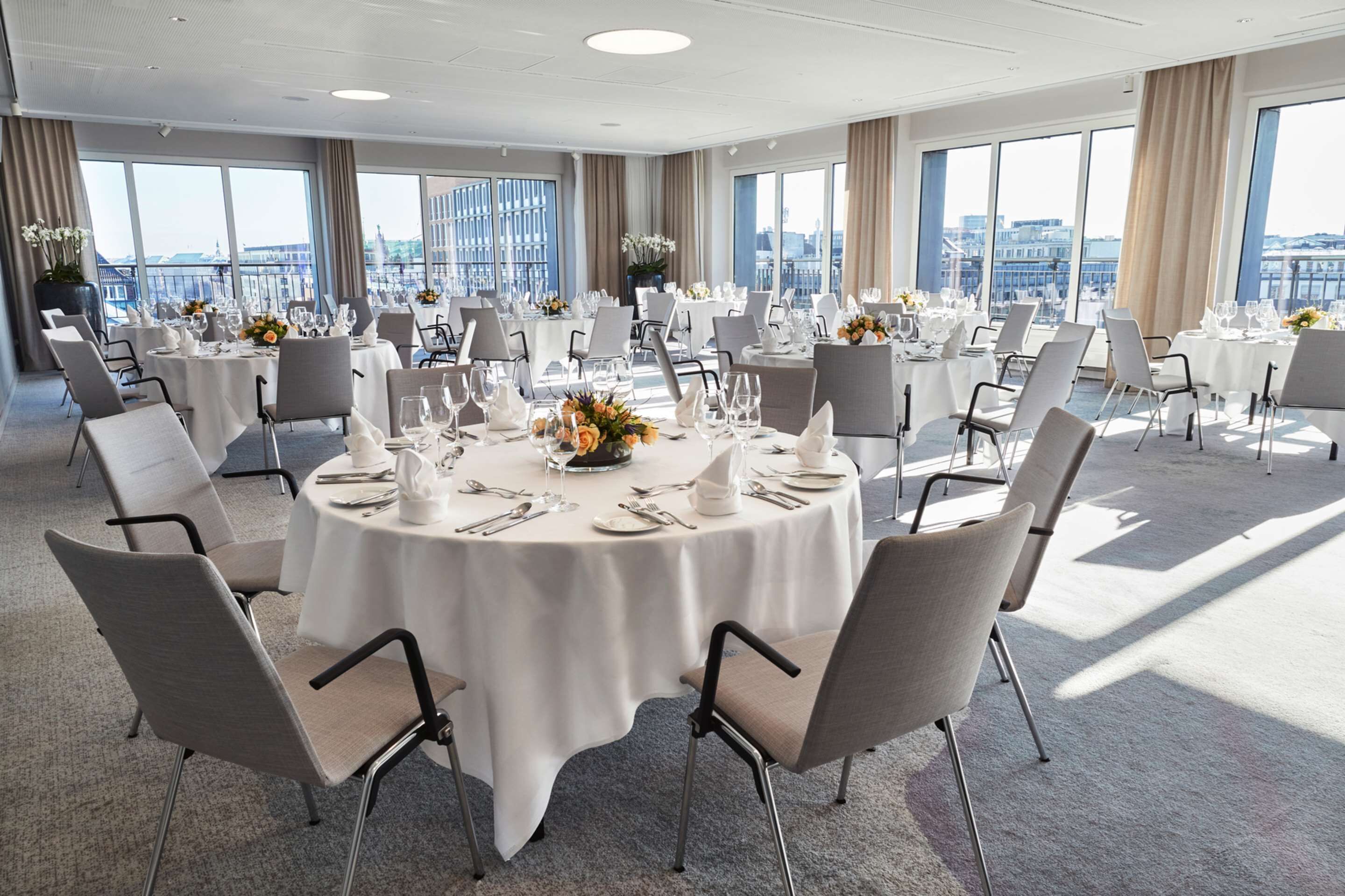 Un salón de conferencias con mesas redondas, sillas y vistas a la ciudad.