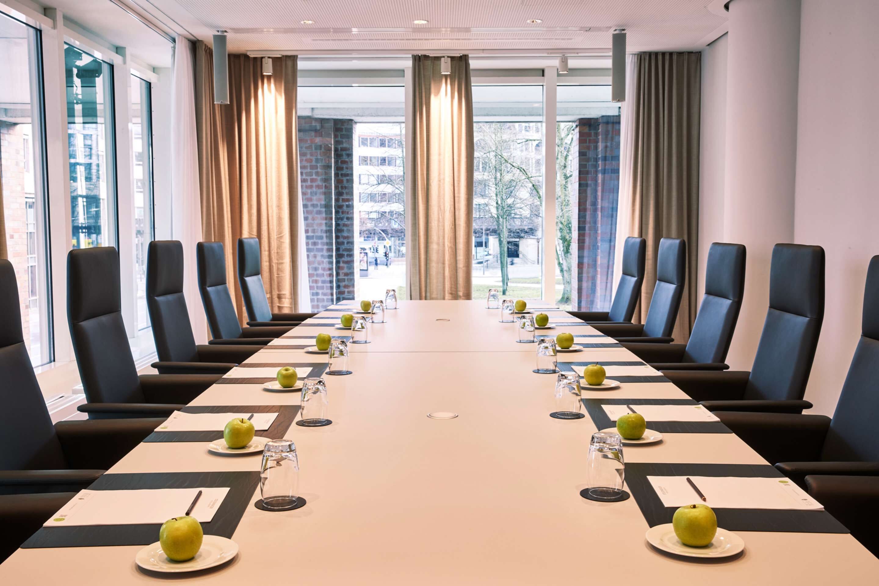 A conference room with a long table, chairs, and apples on plates.