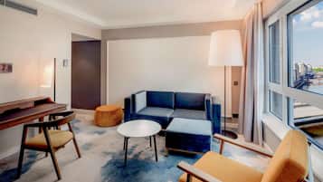 Une chambre d’hôtel moderne équipée d’un canapé, d’un fauteuil, d’un pouf et d’un bureau avec une chaise.