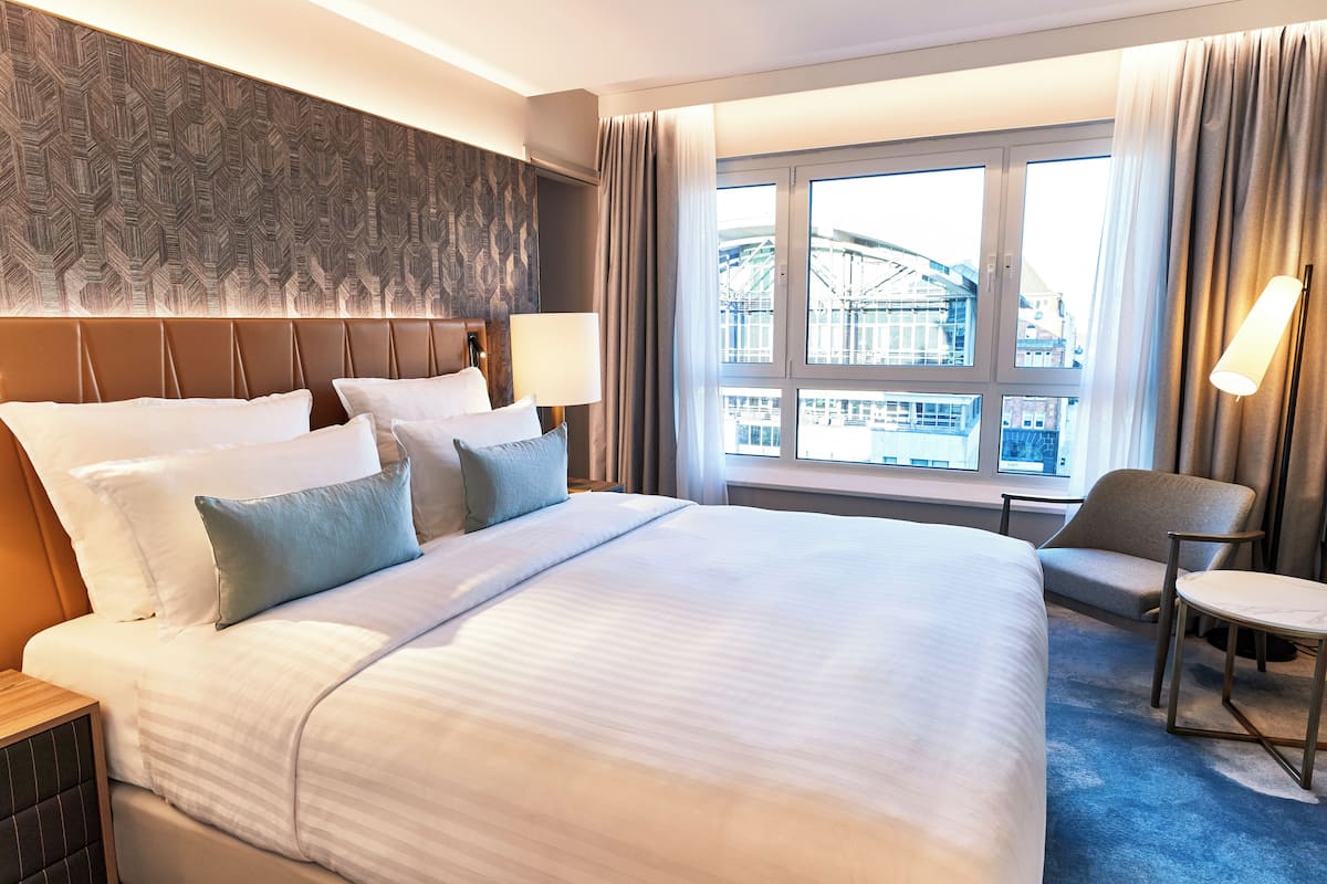 Une chambre d’hôtel avec un grand lit, une chaise, une petite table et une fenêtre donnant sur un immeuble.