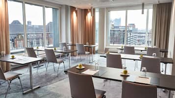 A conference room with multiple tables and chairs, large windows with curtains, and a city view.