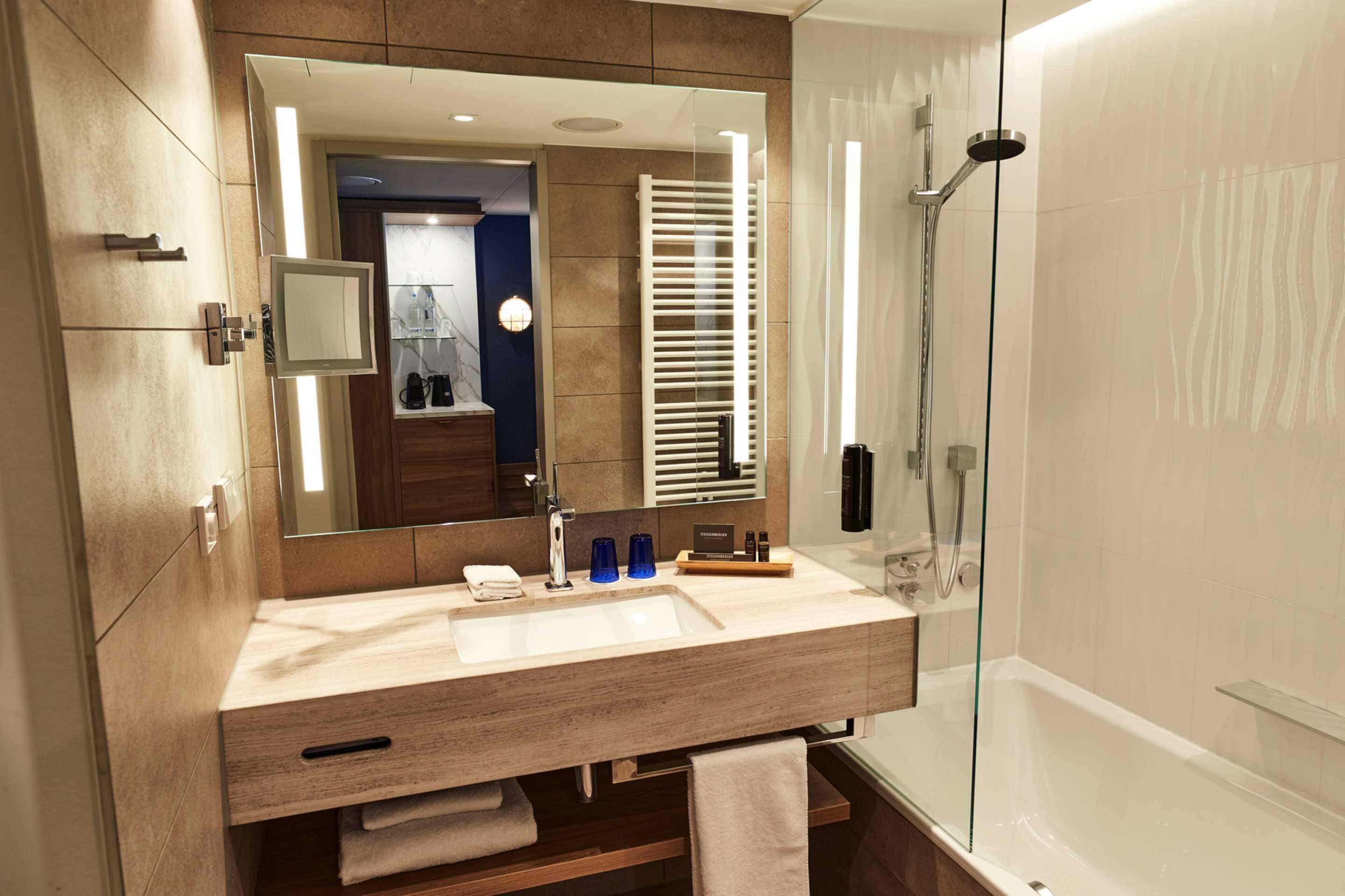 A modern bathroom with a large mirror, a sink, a glass shower enclosure, and a towel rack.