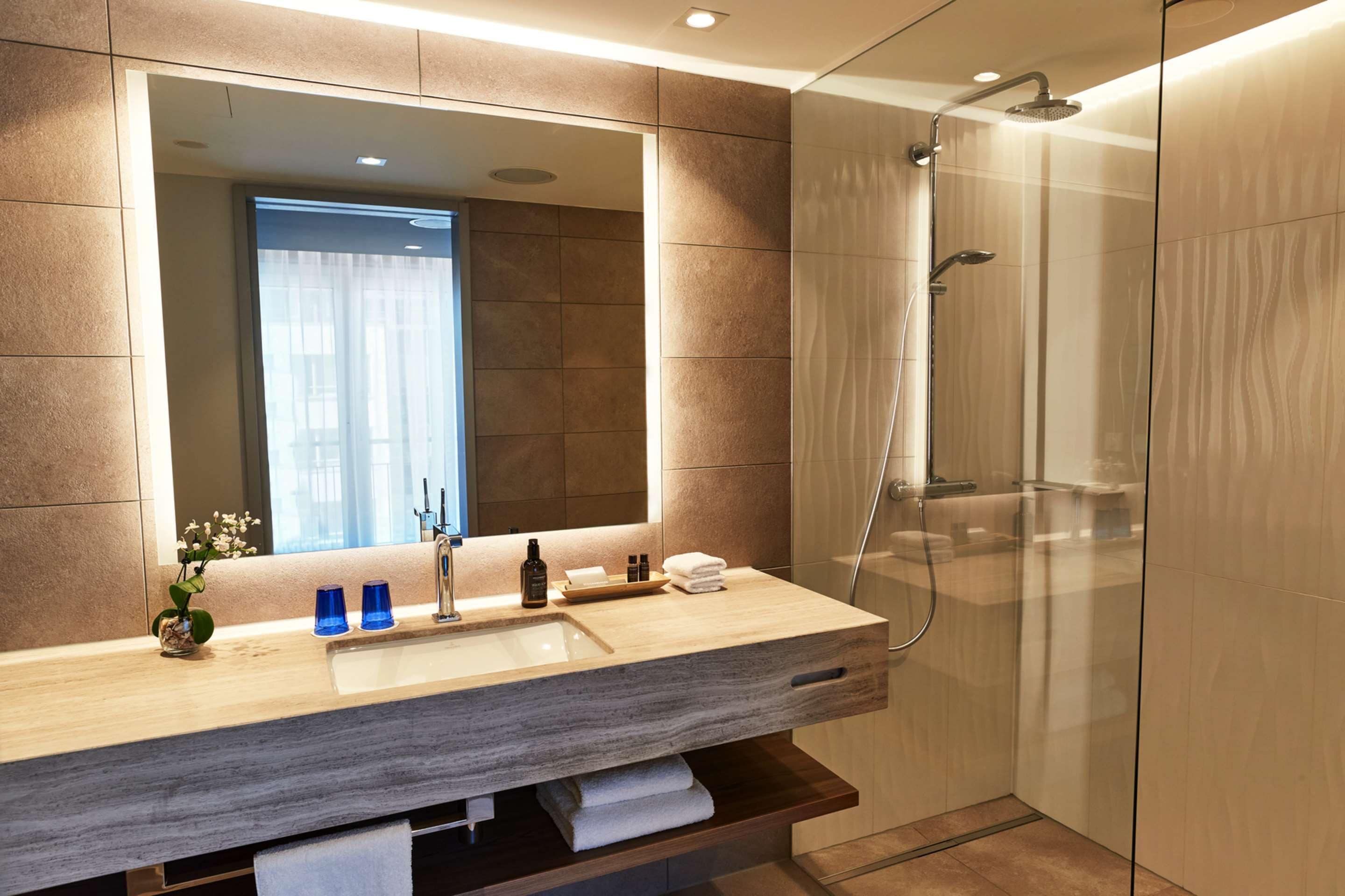 A modern bathroom with a large mirror, a sink, and a glass-enclosed shower.