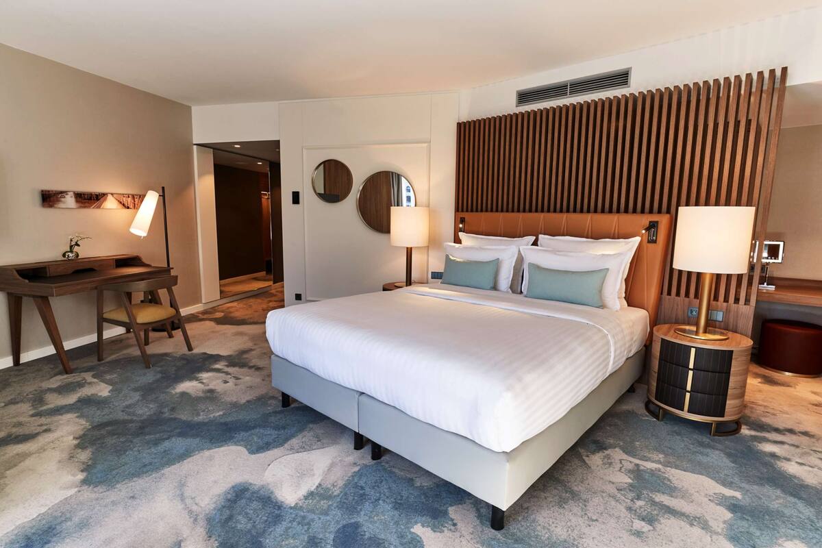 Une chambre d’hôtel avec un grand lit, des lampes de chevet, un bureau et un miroir fixé au mur.