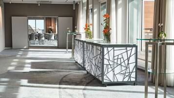 A modern hotel lobby with a glass partition, a seating area with tables and chairs, and a view of the outside.