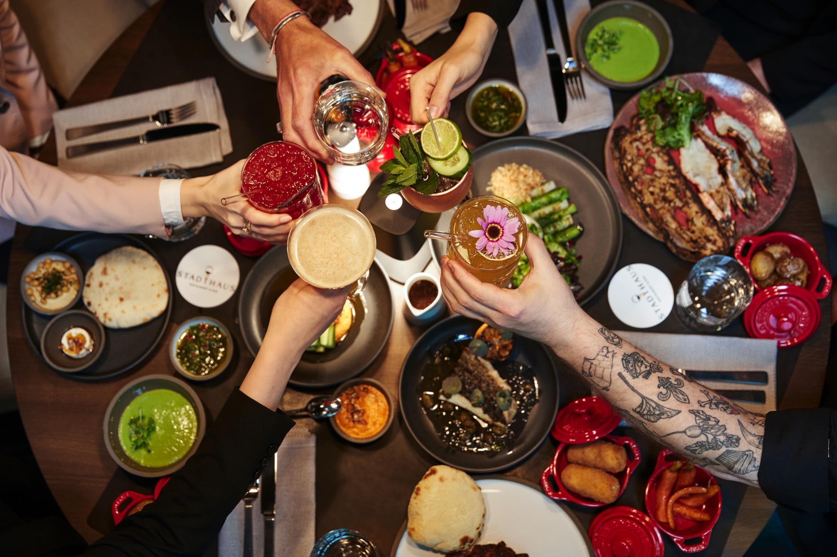 A group of people toasting with drinks at a table with various dishes and condiments.