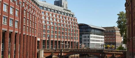 A red brick building with a modern glass extension, a bridge over a canal, and a clear blue sky.