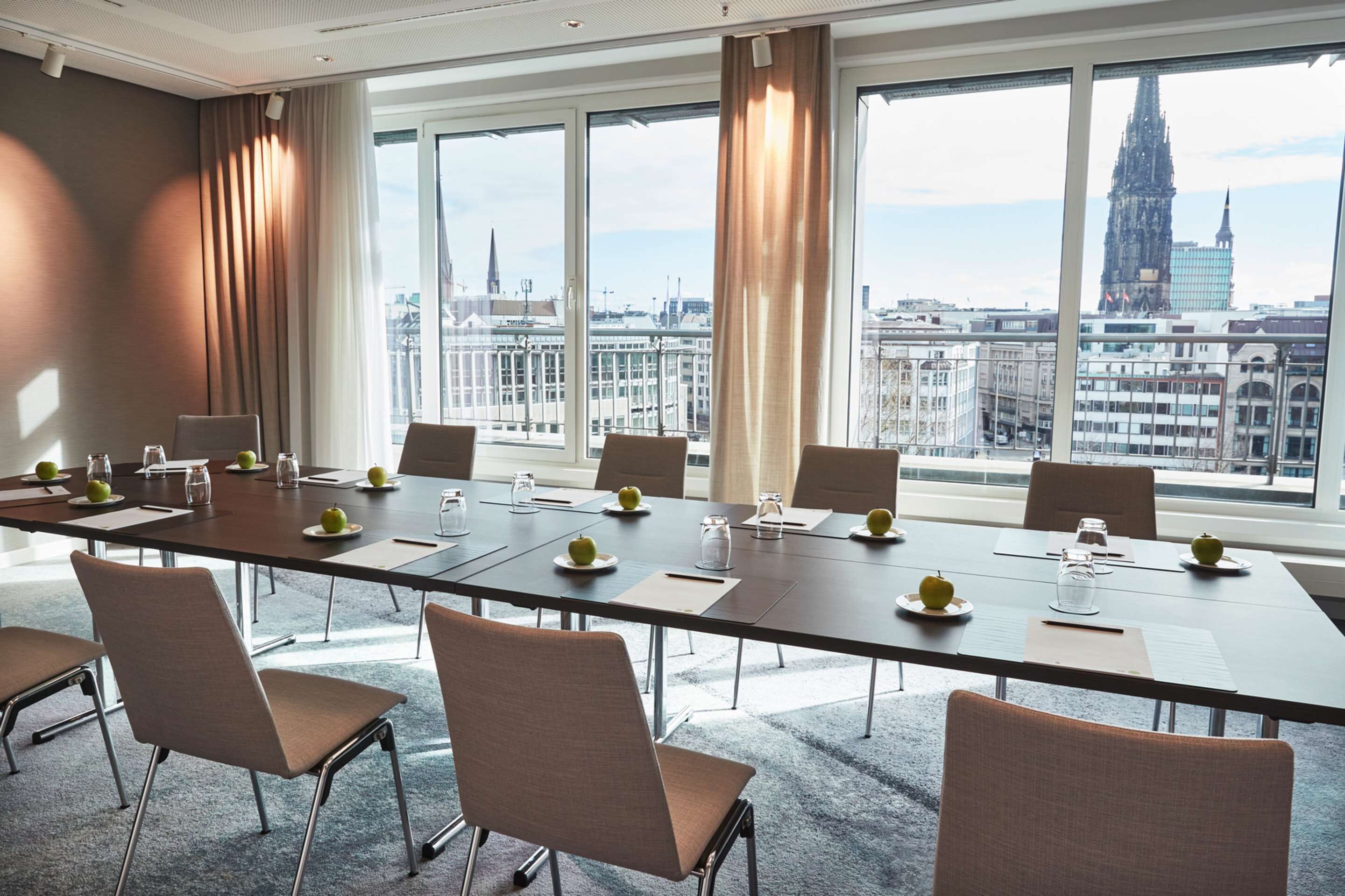 Un salón de conferencias con una larga mesa, sillas y vistas a un paisaje urbano que incluye una catedral.