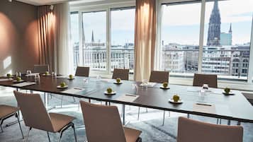 Un salón de conferencias con una larga mesa, sillas y vistas a un paisaje urbano que incluye una catedral.