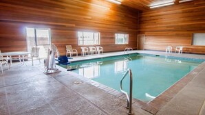 An indoor swimming pool with wooden walls, a tiled floor, and several white chairs around the pool.