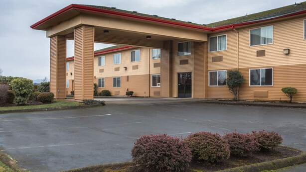 A multi-story hotel with a flat roof, a covered parking area, and a well-maintained landscape with shrubs.