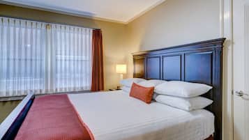 A hotel room with a large bed, a nightstand with a lamp, and a window with curtains.