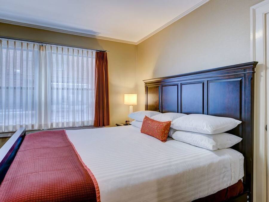 Una habitación de hotel con una cama grande, una mesita de noche con una lámpara y una ventana con cortinas.