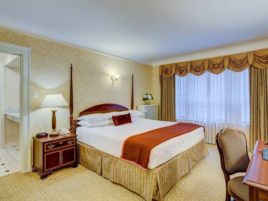 A hotel room with a large bed, a desk, a chair, a nightstand, a lamp, and a mirror.