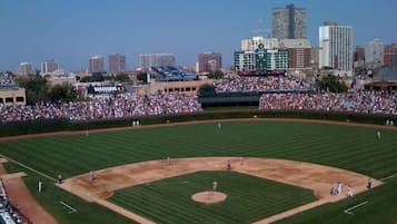 Un estadio de béisbol con una gran multitud, cielo despejado y edificios de la ciudad al fondo.