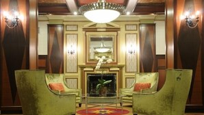 A lobby with two green armchairs, a glass coffee table, a chandelier, and a fireplace.
