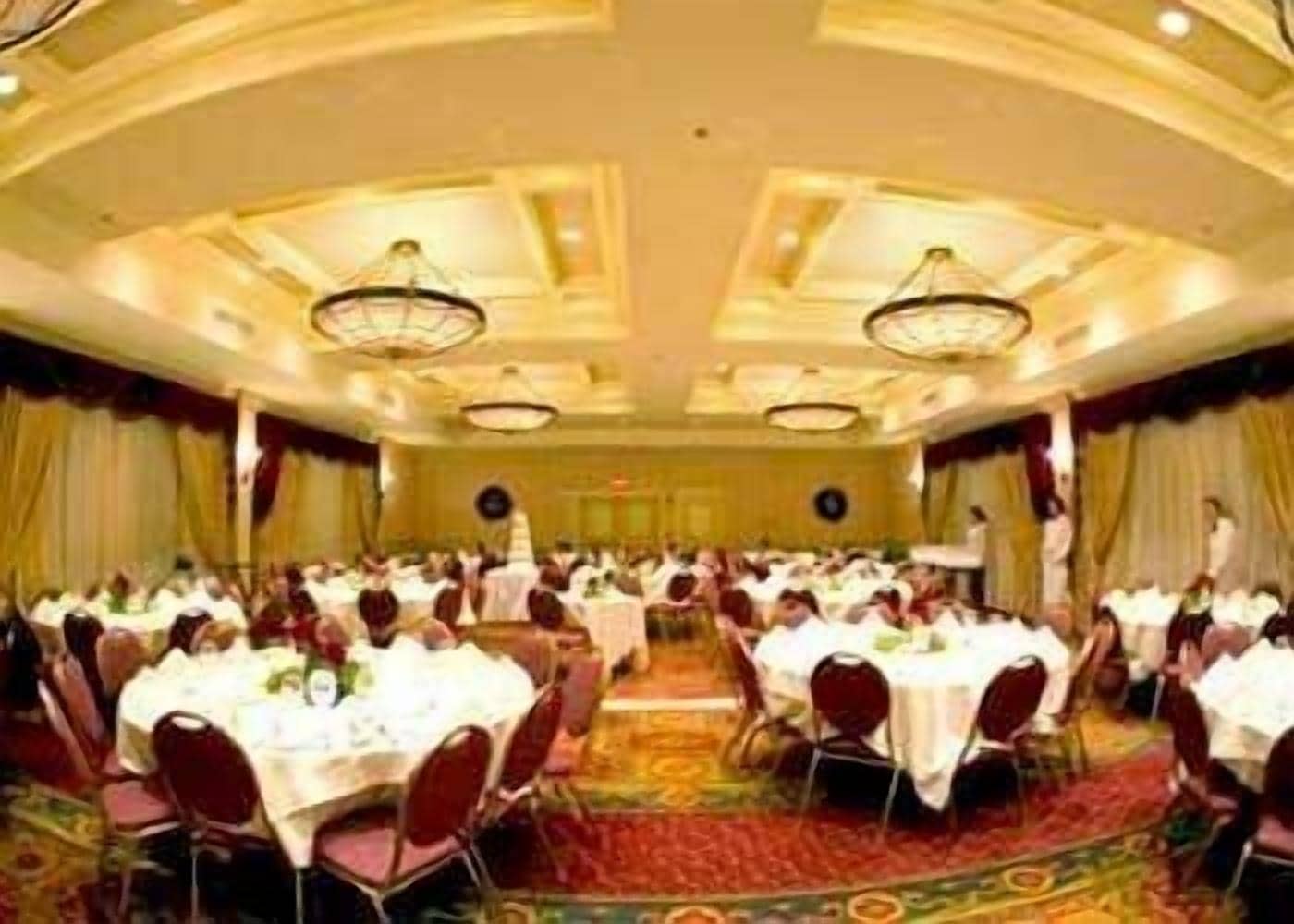 Un salón de banquetes con mesas redondas, sillas y suelo alfombrado.