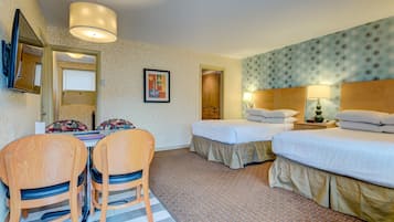 A hotel room with two beds, a dining table with chairs, a mirror, and a wall-mounted TV.