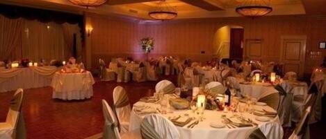 A banquet hall with round tables, white tablecloths, and chairs with green sashes.