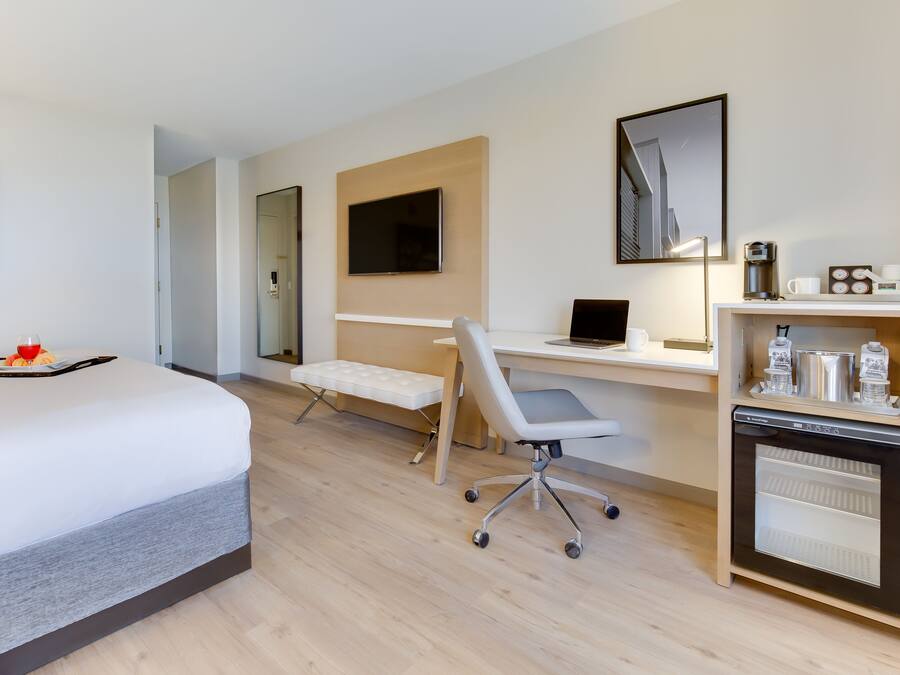 Habitación de hotel con cama, escritorio con computadora portátil, silla, refrigerador pequeño y cafetera.