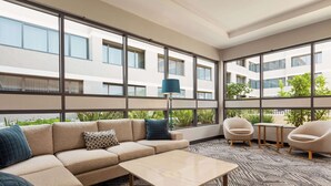 Una habitación de hotel moderna con un ventanal grande, un sofá color beige, una mesita pequeña y dos sillas.