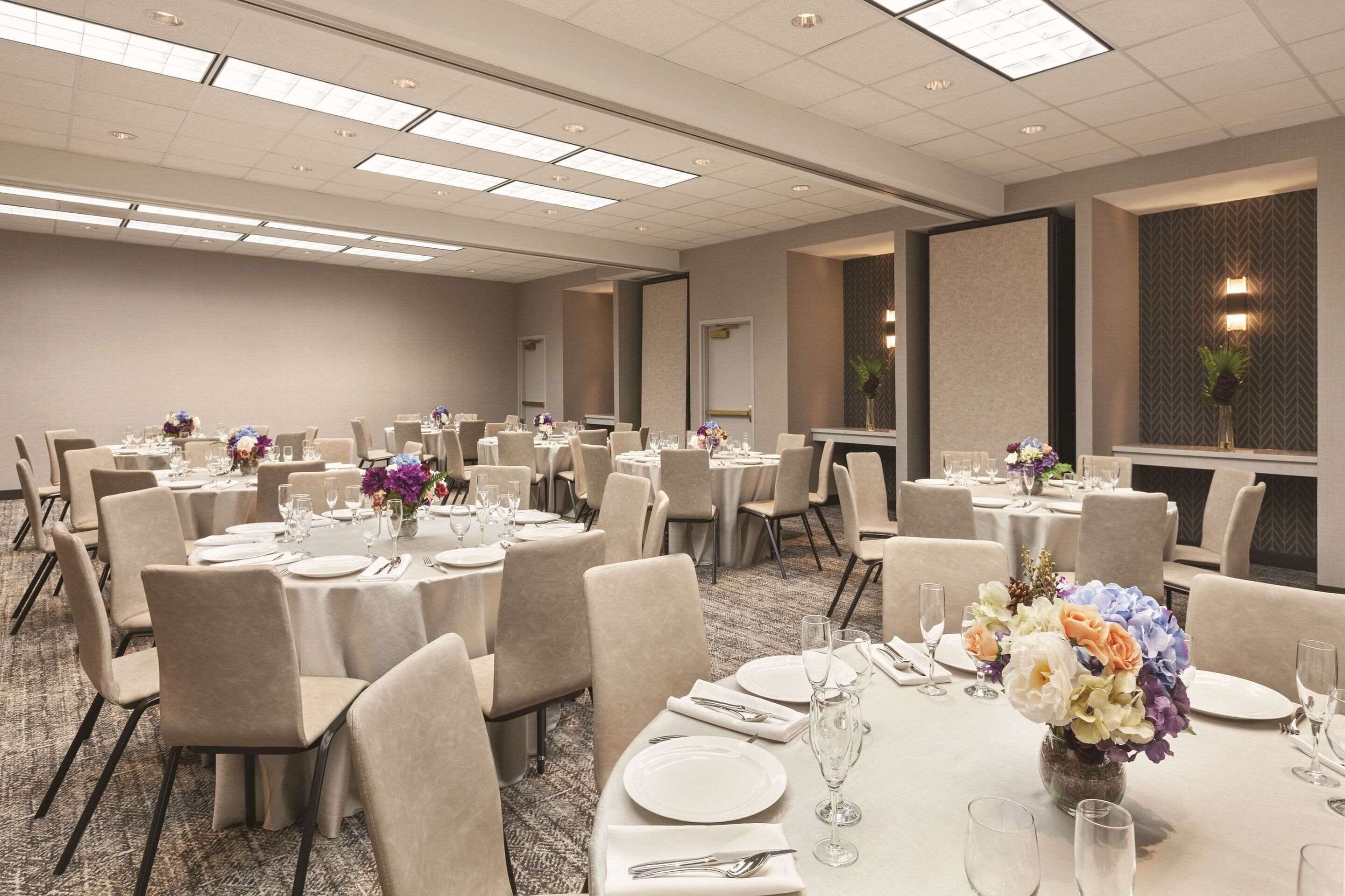Un salón de conferencias con mesas redondas, sillas y centros de mesa florales.