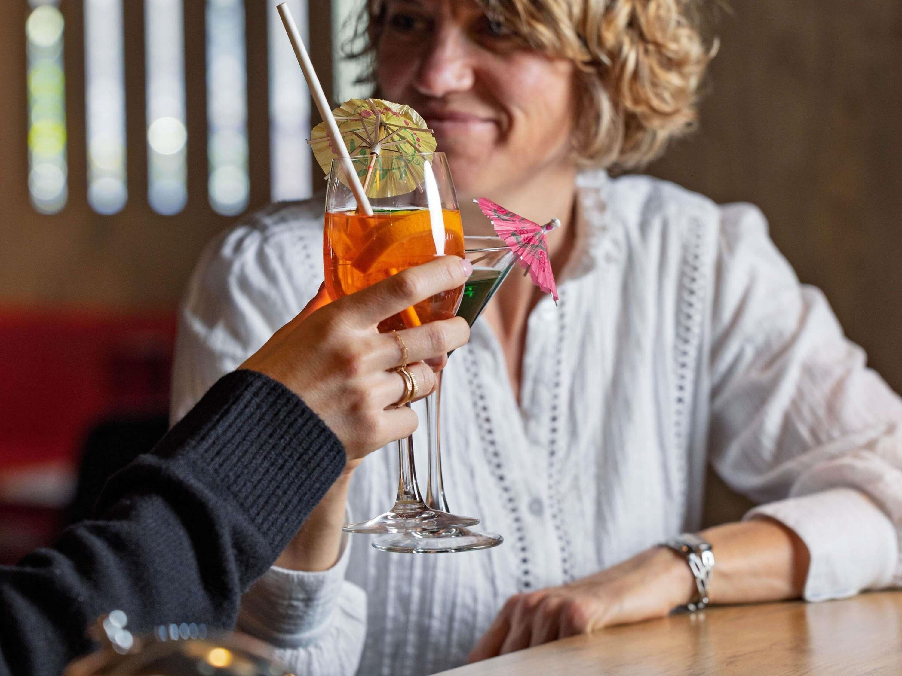 Eine Person hält ein Cocktailglas mit einem Strohhalm und einem Zier-Regenschirm.