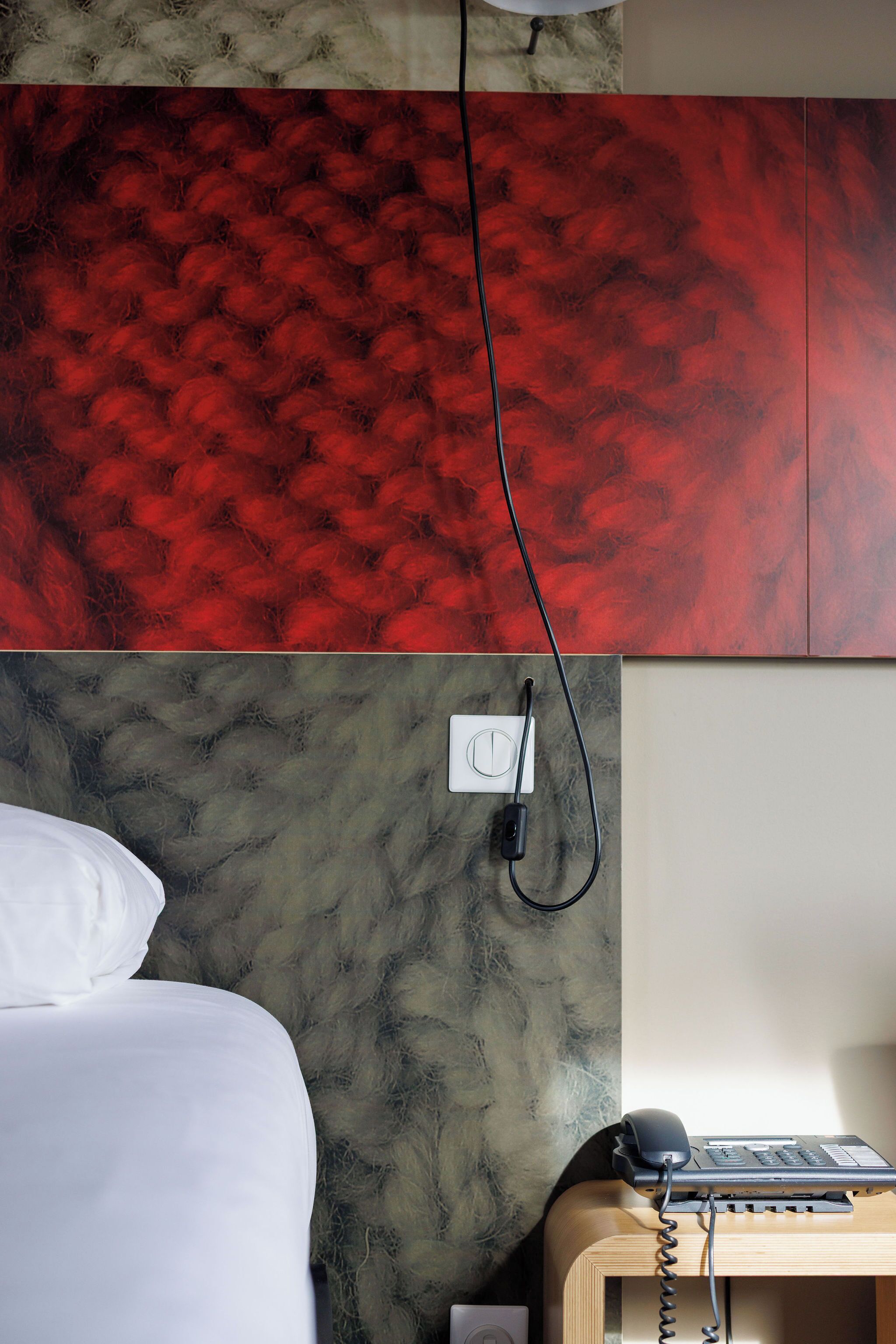 A hotel room with a bed, a telephone, and a wall-mounted power outlet.