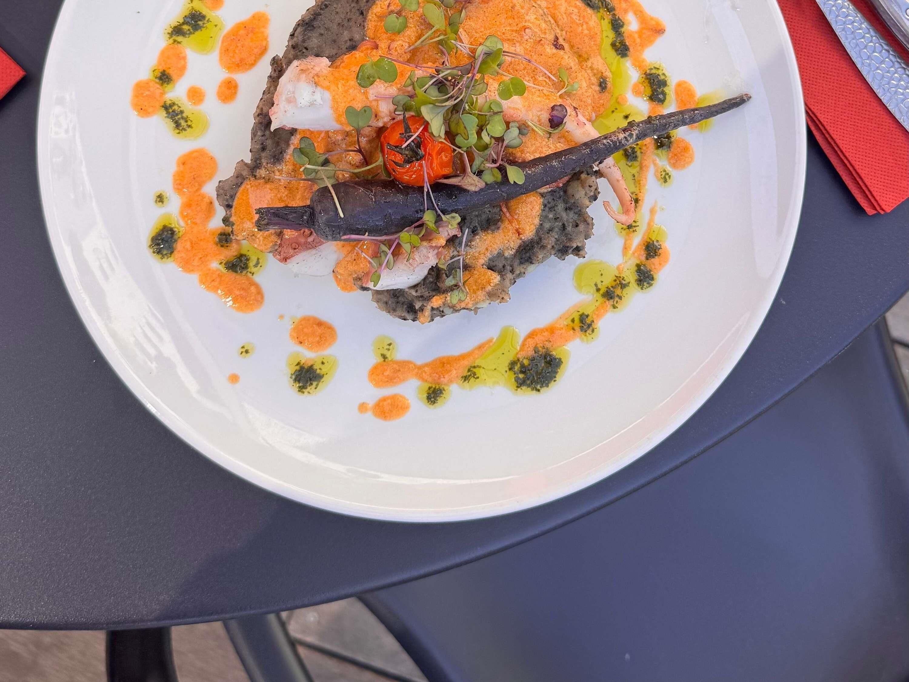A white plate with a seafood dish, garnished with microgreens and a sauce, on a dark table.