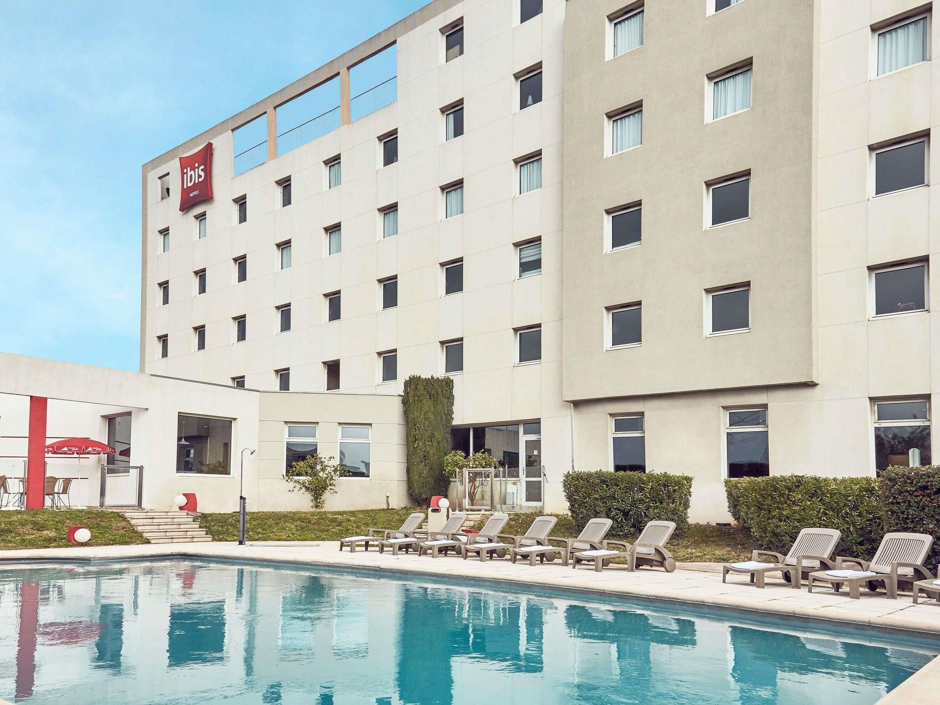 A hotel with a swimming pool, lounge chairs, and a red ibis logo.