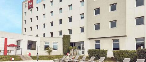 A hotel with a swimming pool, lounge chairs, and a red ibis logo.