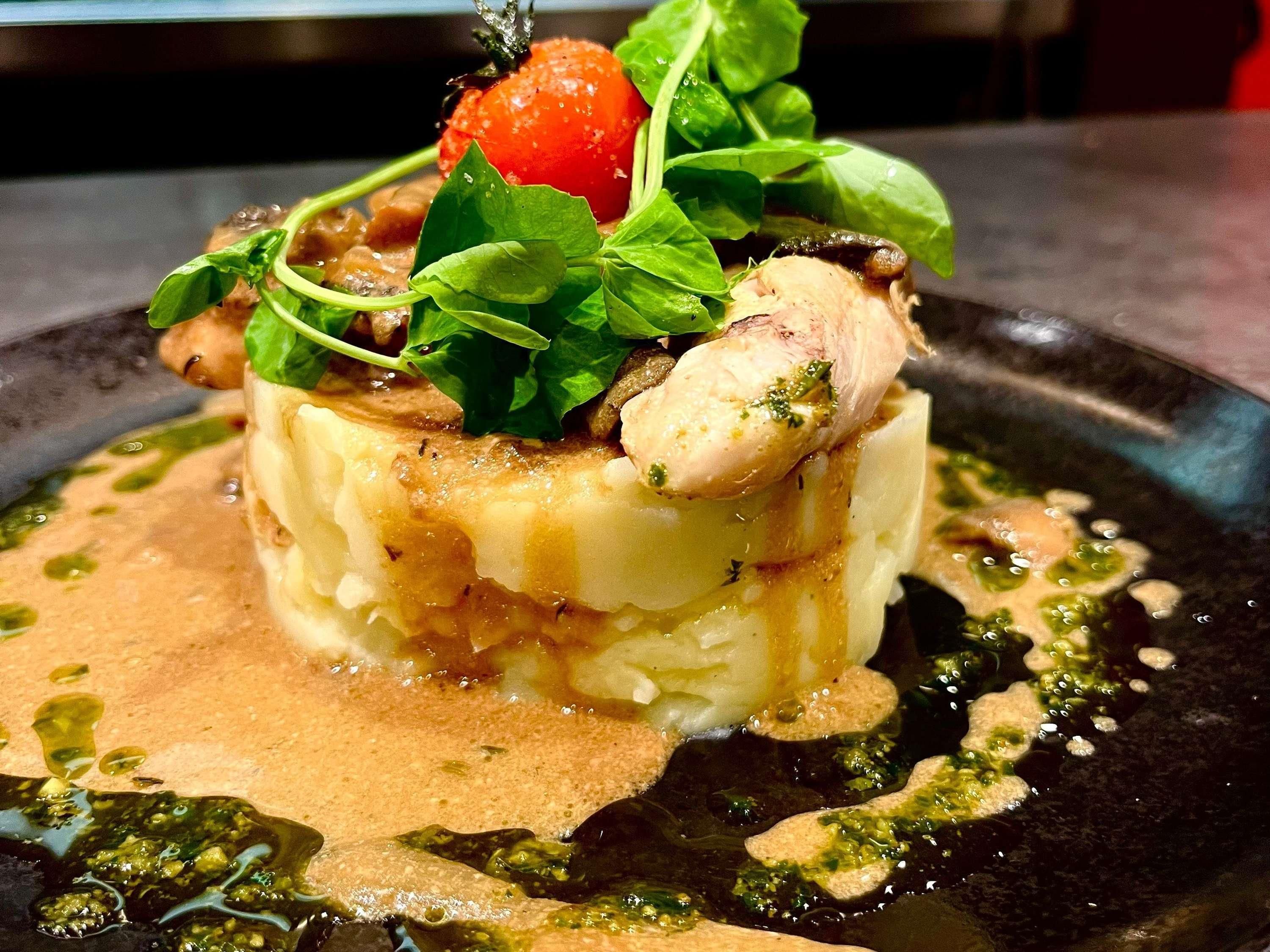 A plated dish with a cherry, greens, and a creamy sauce.