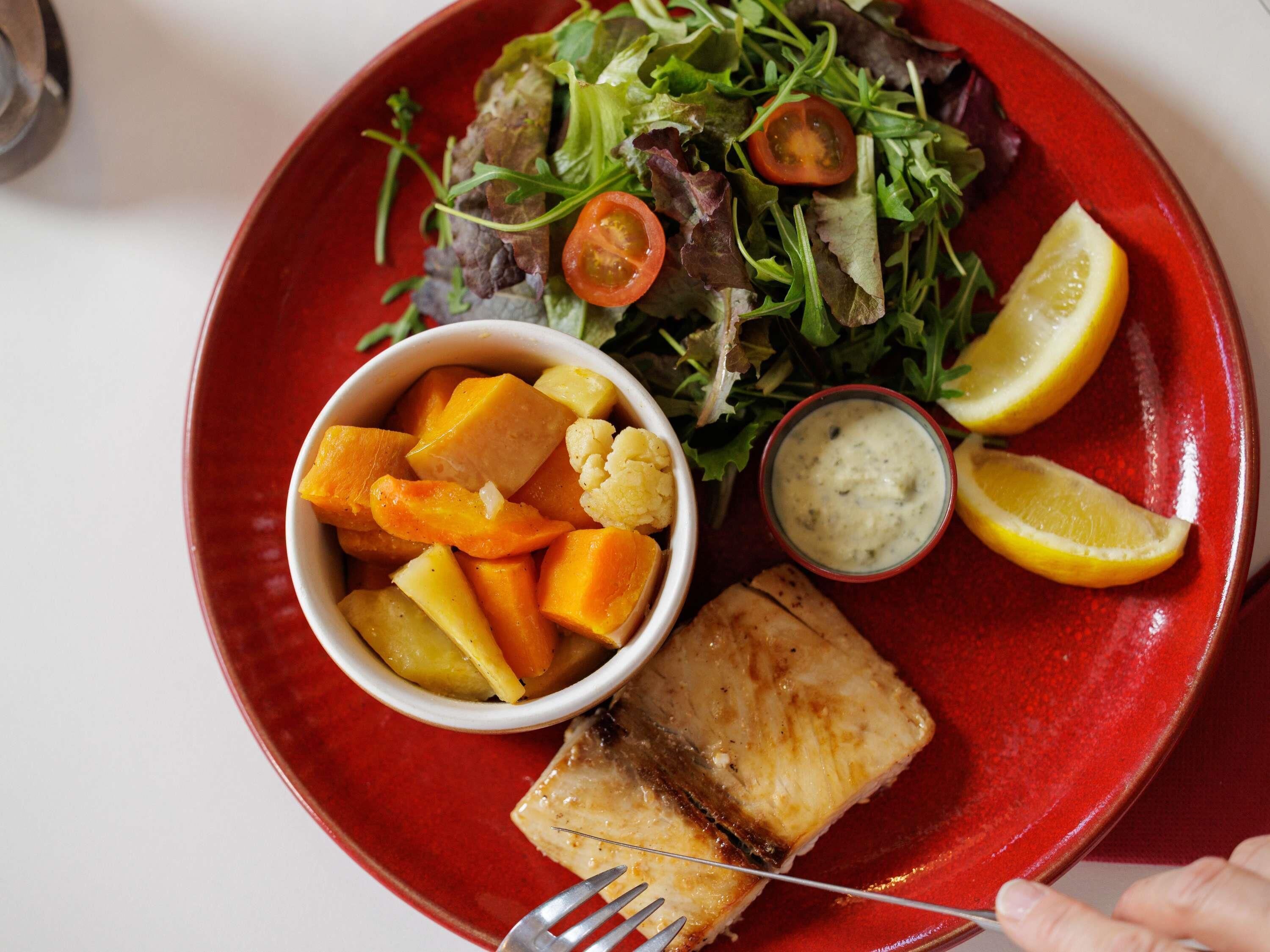 Une assiette avec un morceau de poisson, une salade et un bol de légumes.