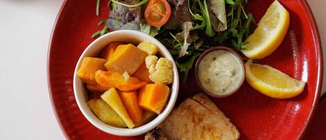 Une assiette avec un morceau de poisson, une salade et un bol de légumes.