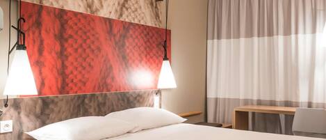 A hotel room with a bed, two bedside lamps, a desk, and a chair.