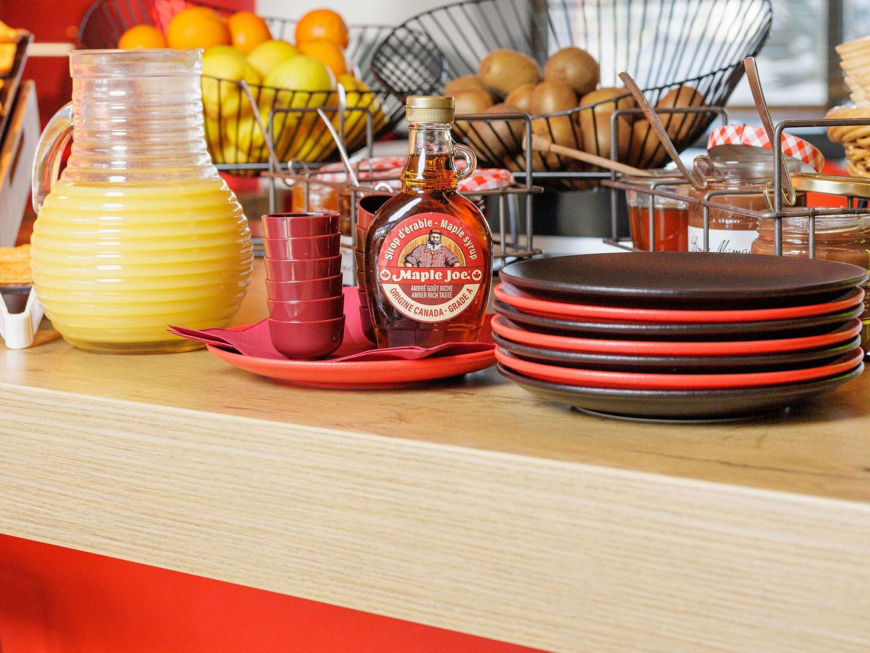 A breakfast setup with maple syrup, a pitcher, and a bowl of fruits.