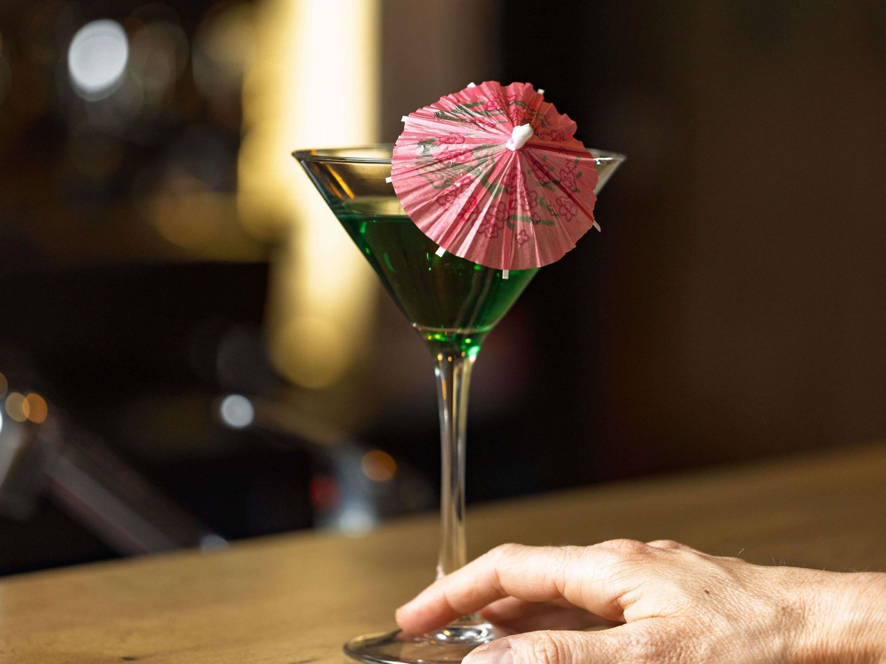Un verre à martini avec un petit parasol rose, posé sur le comptoir en bois d’un bar.