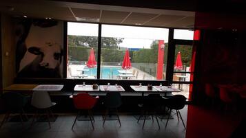 Area pranzo interna con vista sulla piscina, ombrelloni rossi e sedie moderne.