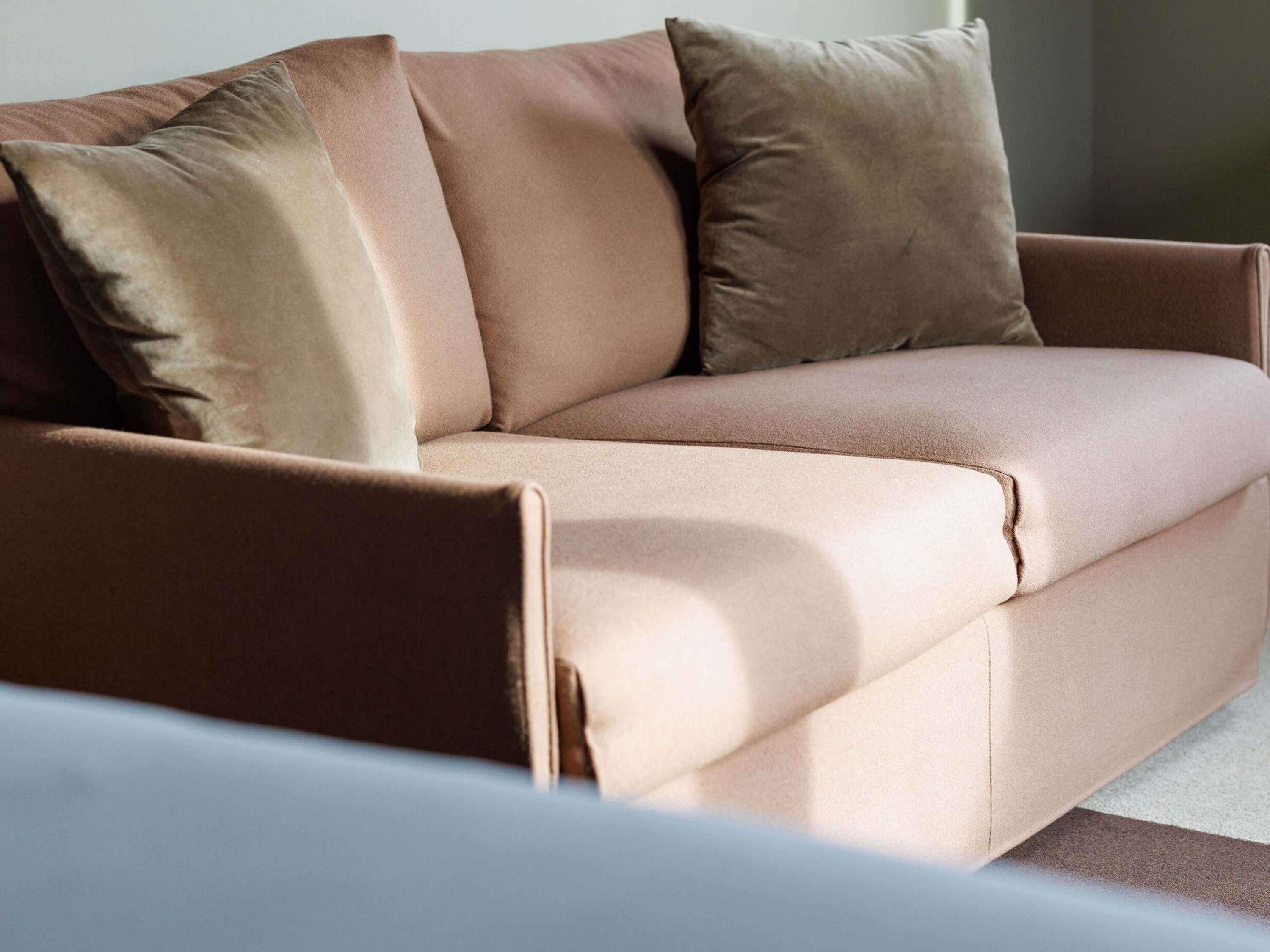 A modern sofa with a light brown fabric and a dark brown cushion.