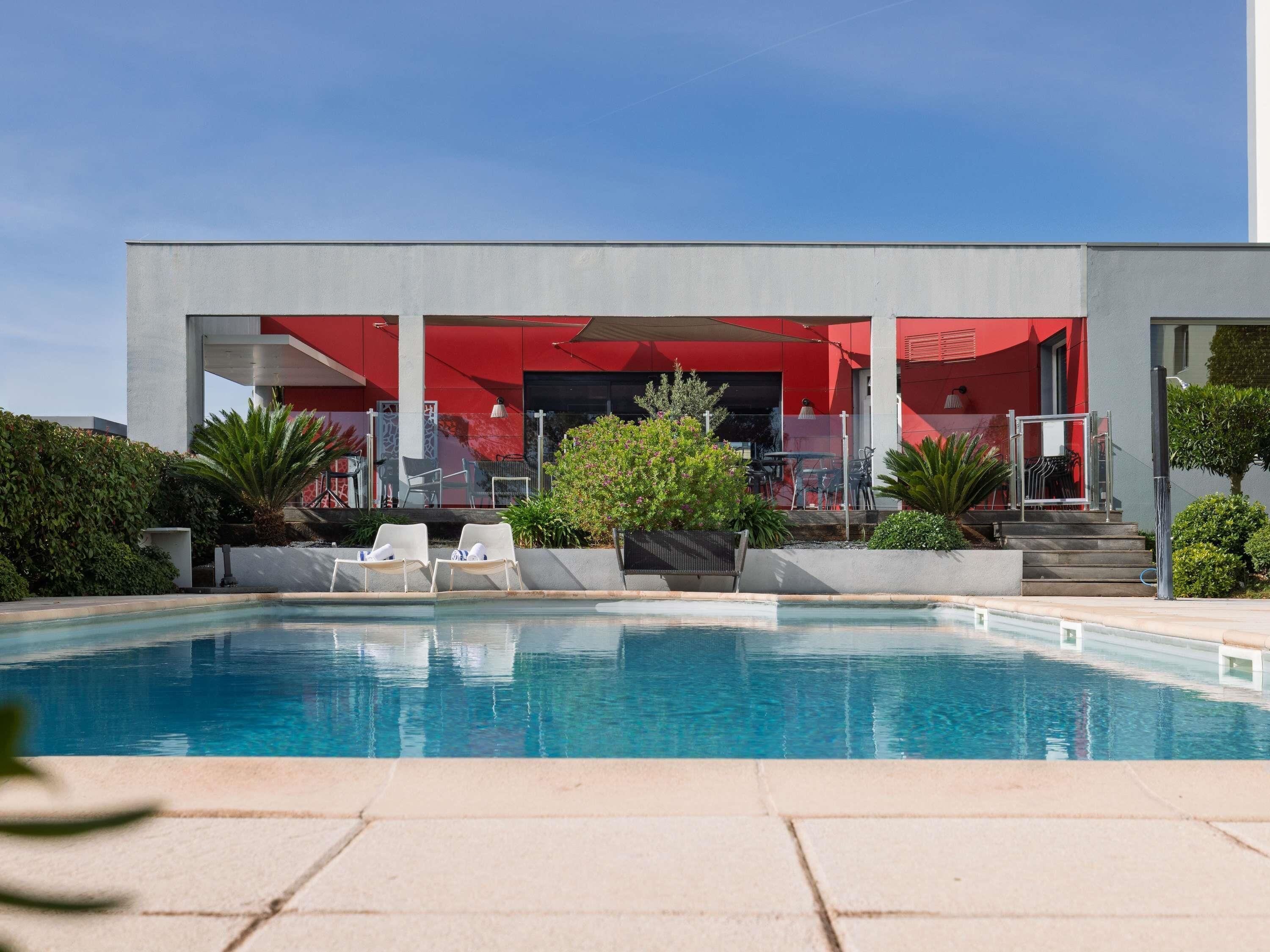 A modern hotel with a swimming pool, outdoor seating, and a red building facade.
