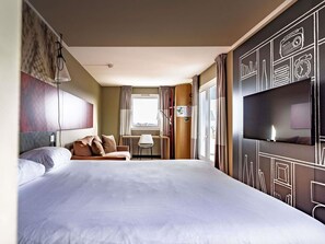 A hotel room with a large bed, a desk, a television, and a window with curtains.