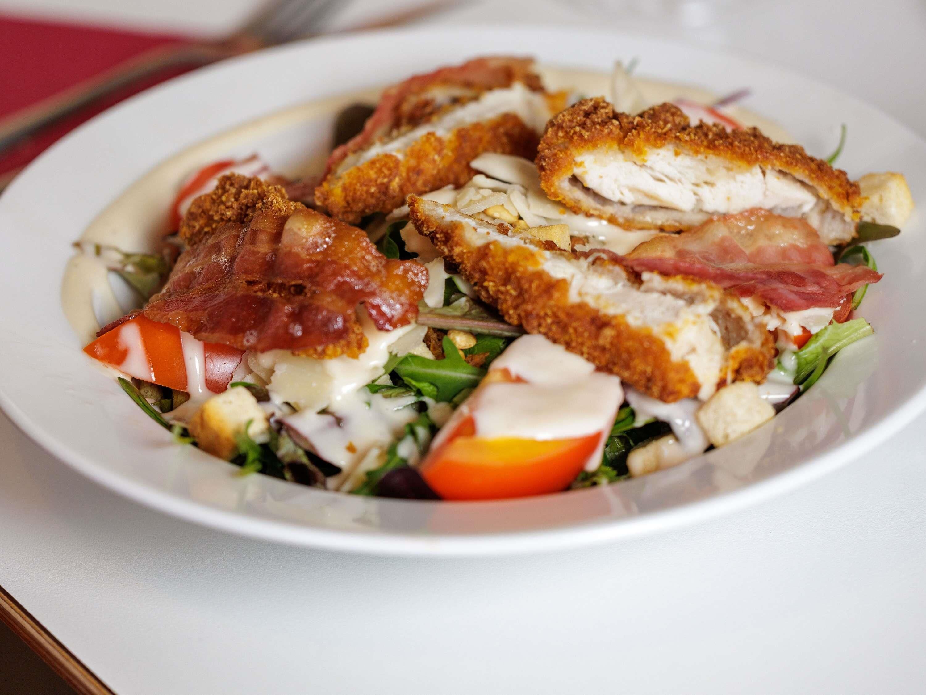 Un plato de comida con ensalada, pollo y tocino.