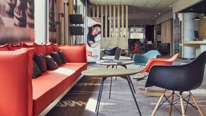 A modern hotel lobby with a red sofa, a round table, and colorful chairs. - ibis Toulon La Valette (La Valette-du-Var)