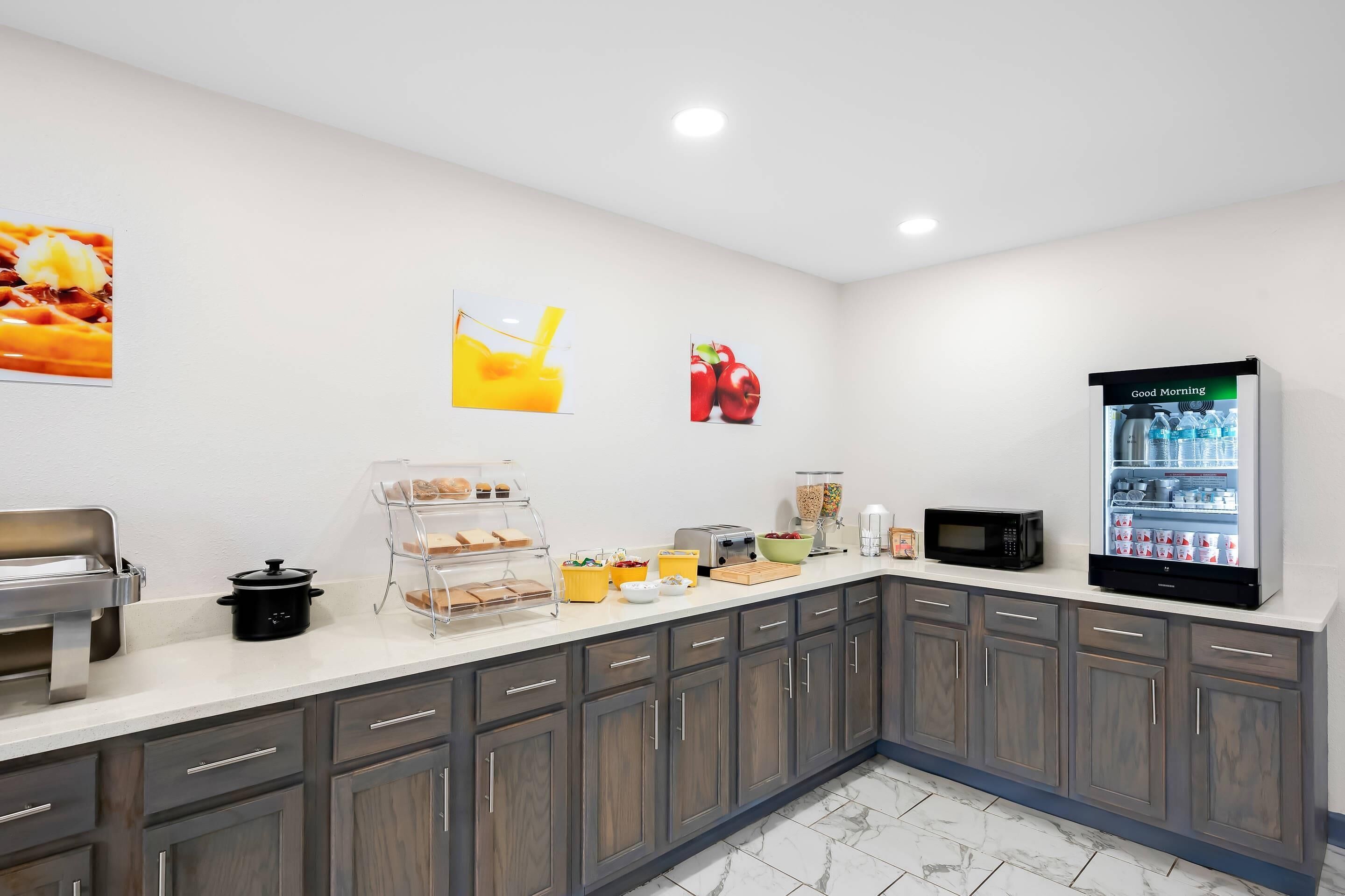 Eine moderne Küche mit weißer Arbeitsplatte, dunklen Holzschränken, einer Mikrowelle, einem Kühlschrank und verschiedenen Lebensmitteln und Geräten.