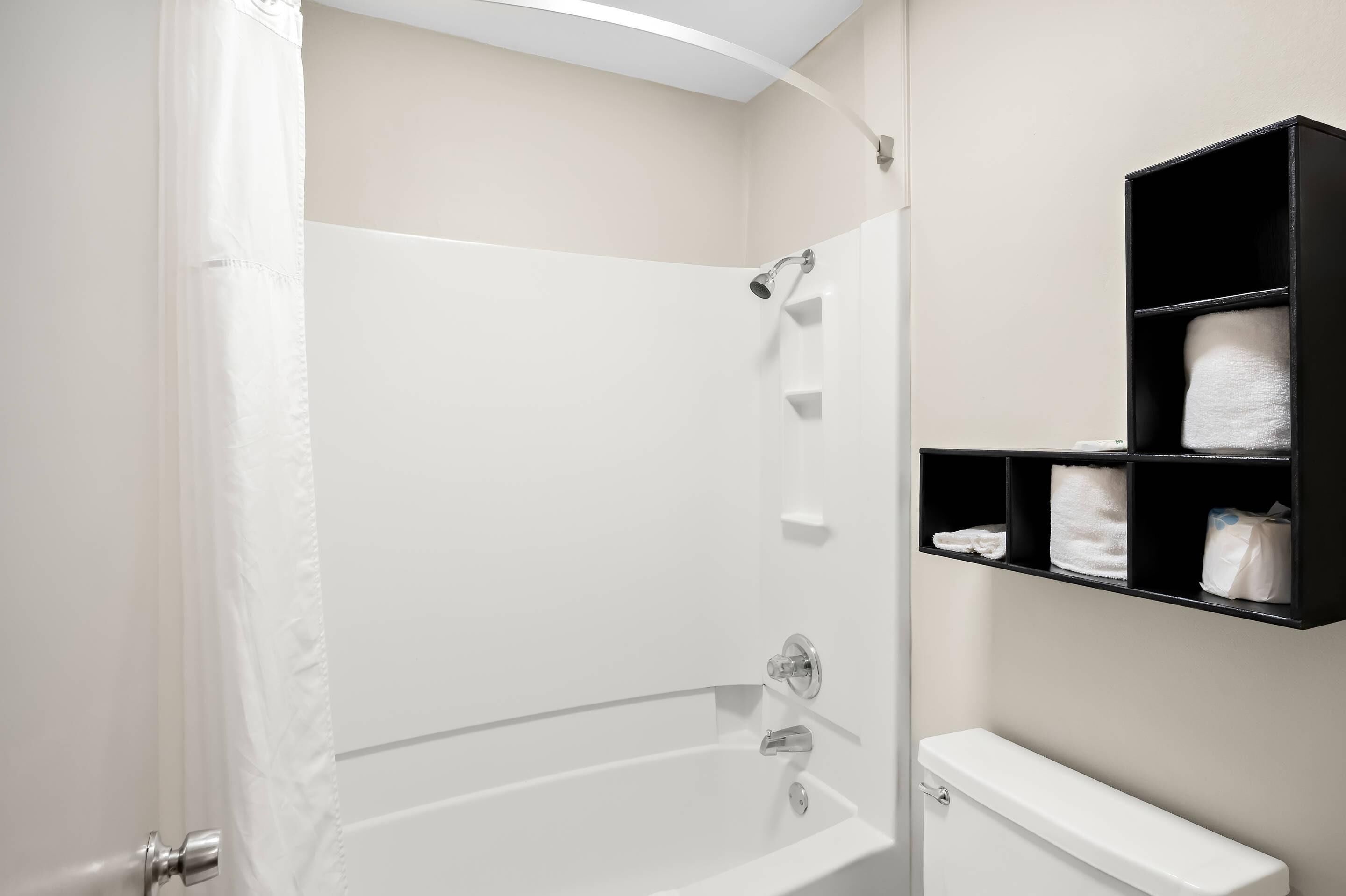 Un baño con bañera, ducha y un estante con toallas.