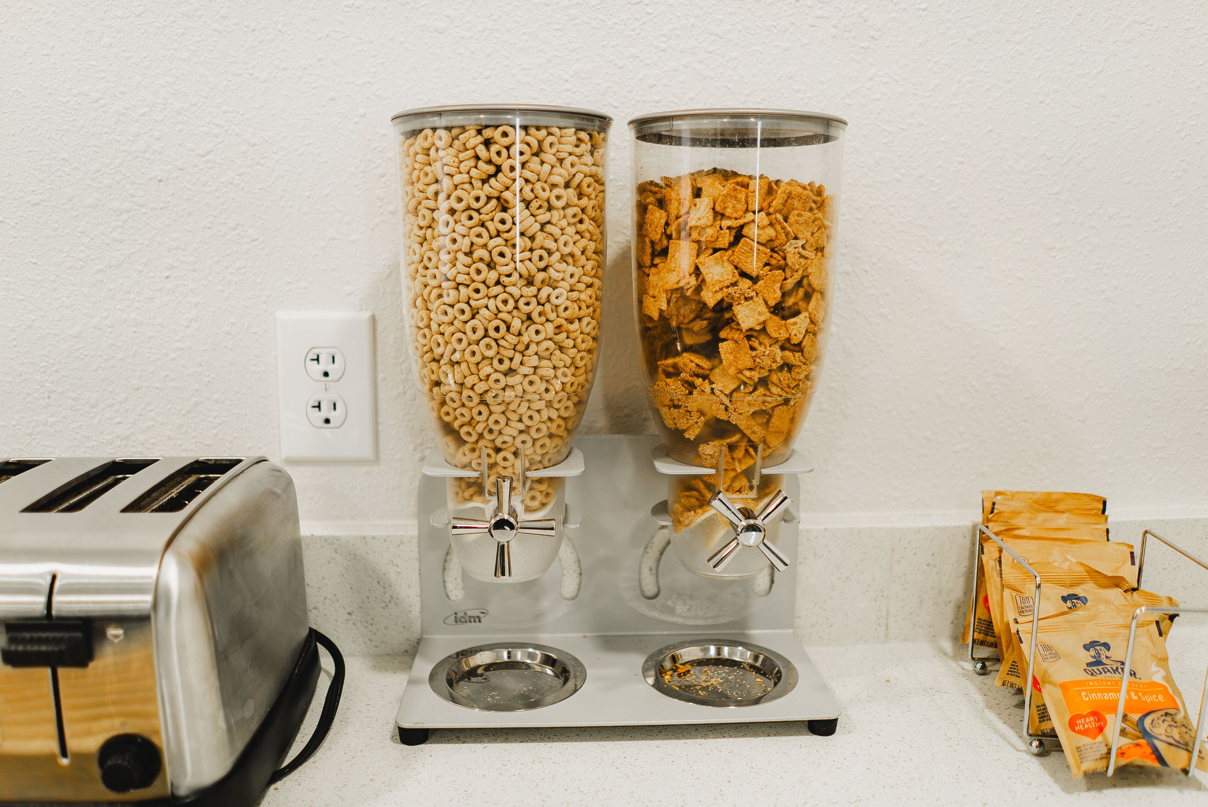 A kitchen with a toaster, two cereal dispensers, and a bag of cinnamon and sugar.