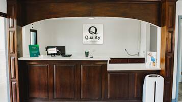 Un mostrador de recepción con un cartel que dice "Quality by Choice Hotels", una computadora, un letrero verde y un cubo de basura blanco.