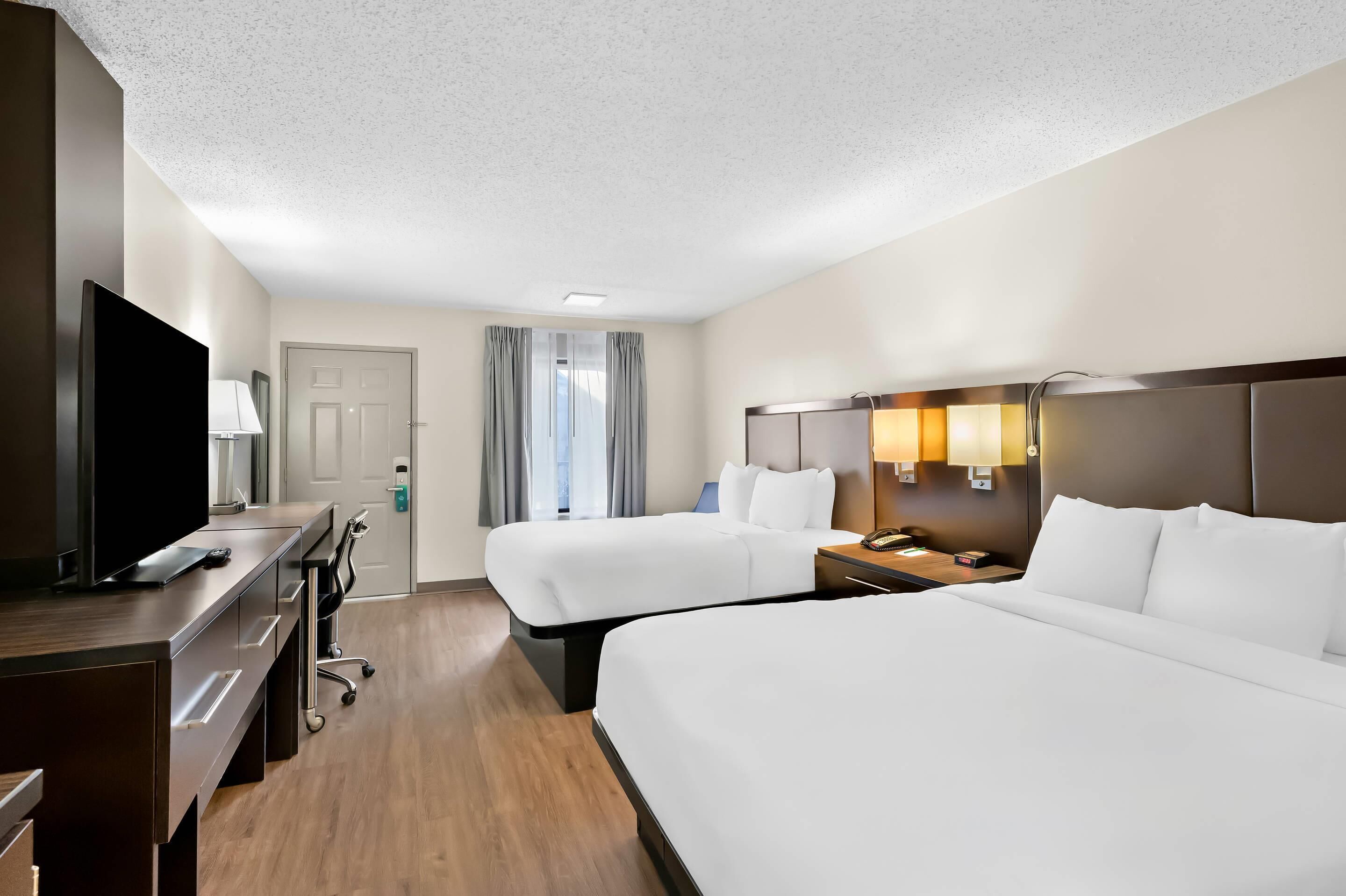 Une chambre d’hôtel avec deux lits, un bureau avec une télévision, une lampe et une porte.