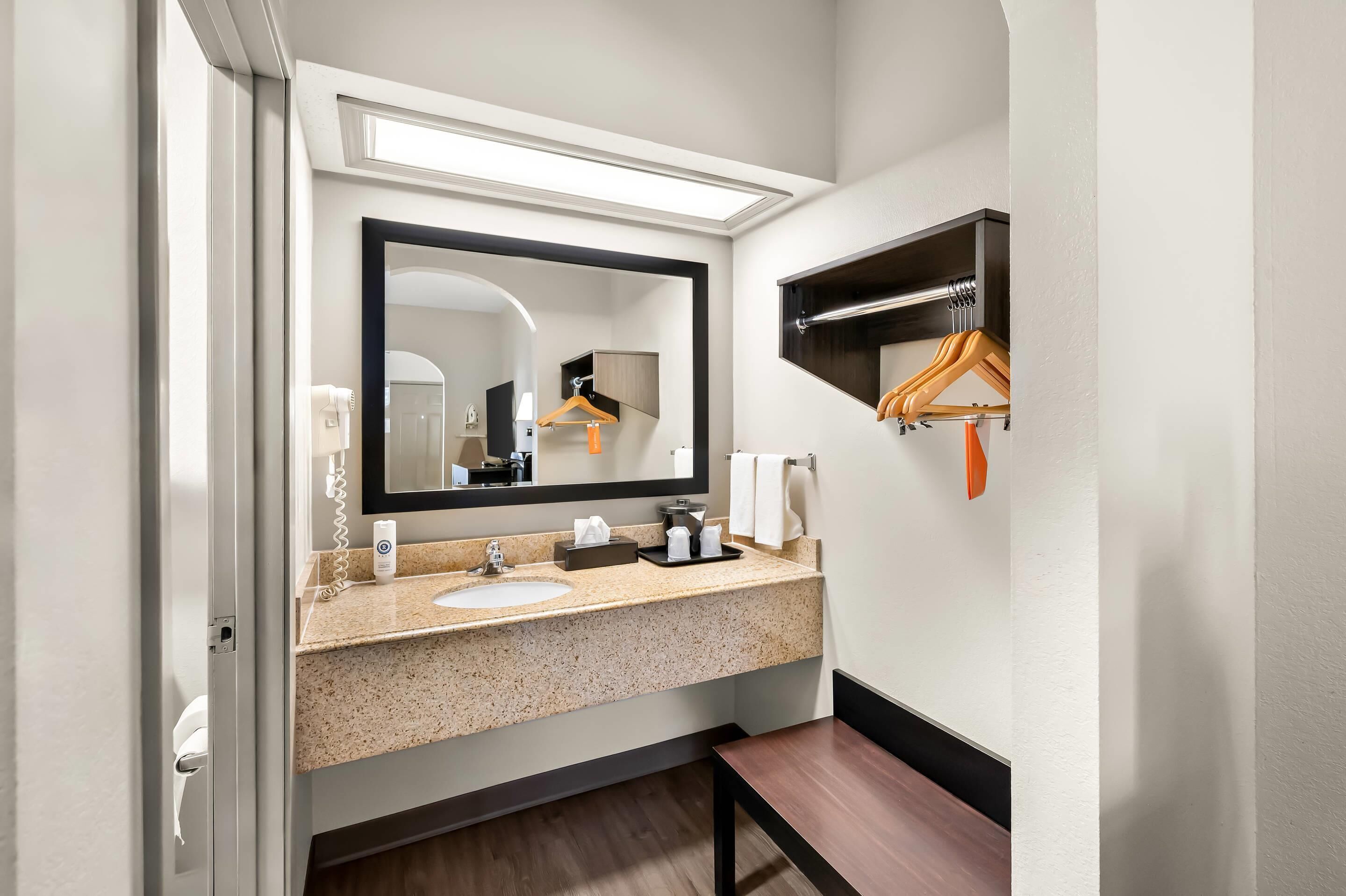 A modern bathroom with a granite countertop sink, a large mirror, a towel rack, and a wooden bench.