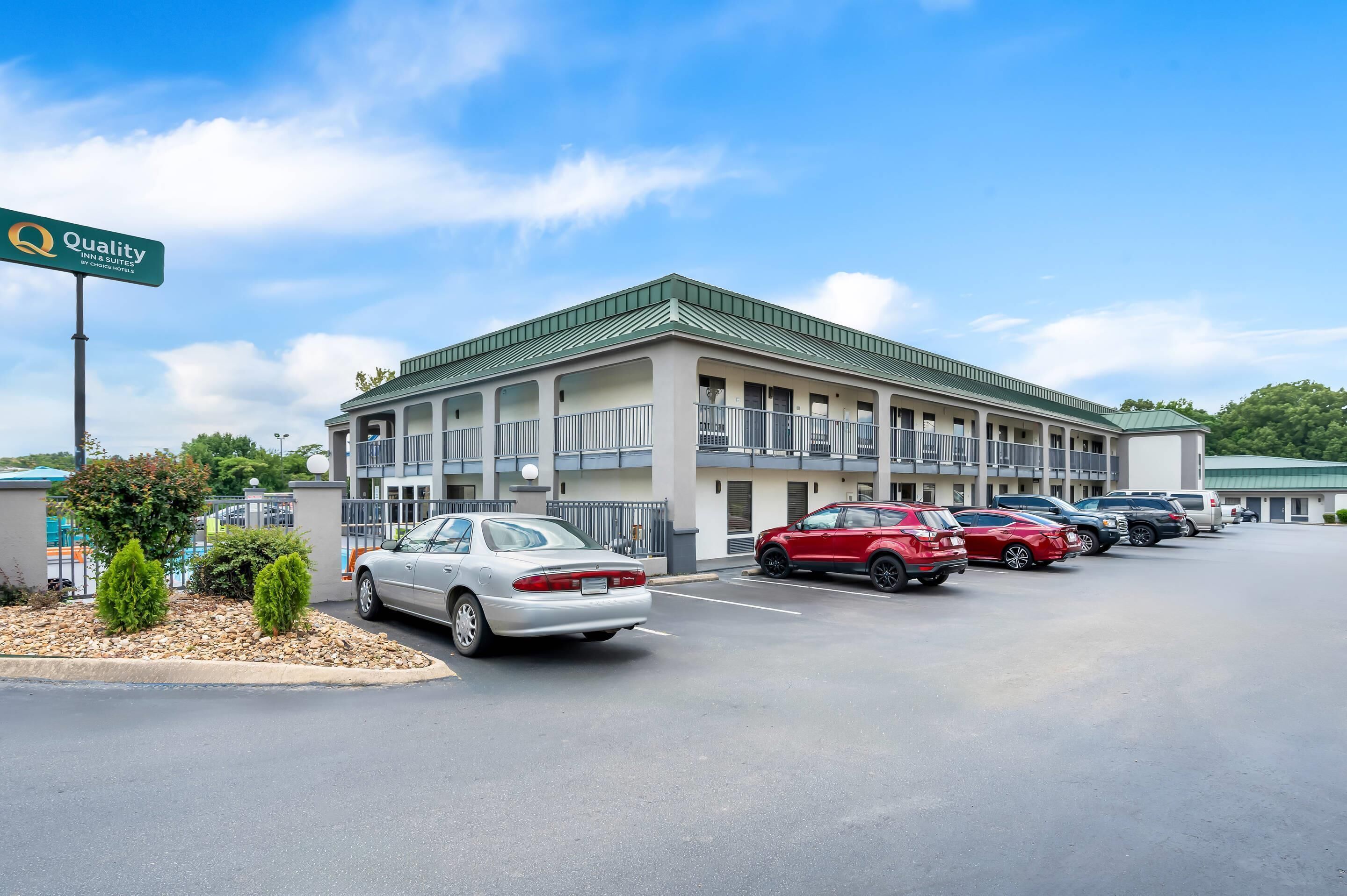 A motel with a green roof and multiple balconies, a parking lot with several cars, and a sign indicating "Quality Inn & Suites."